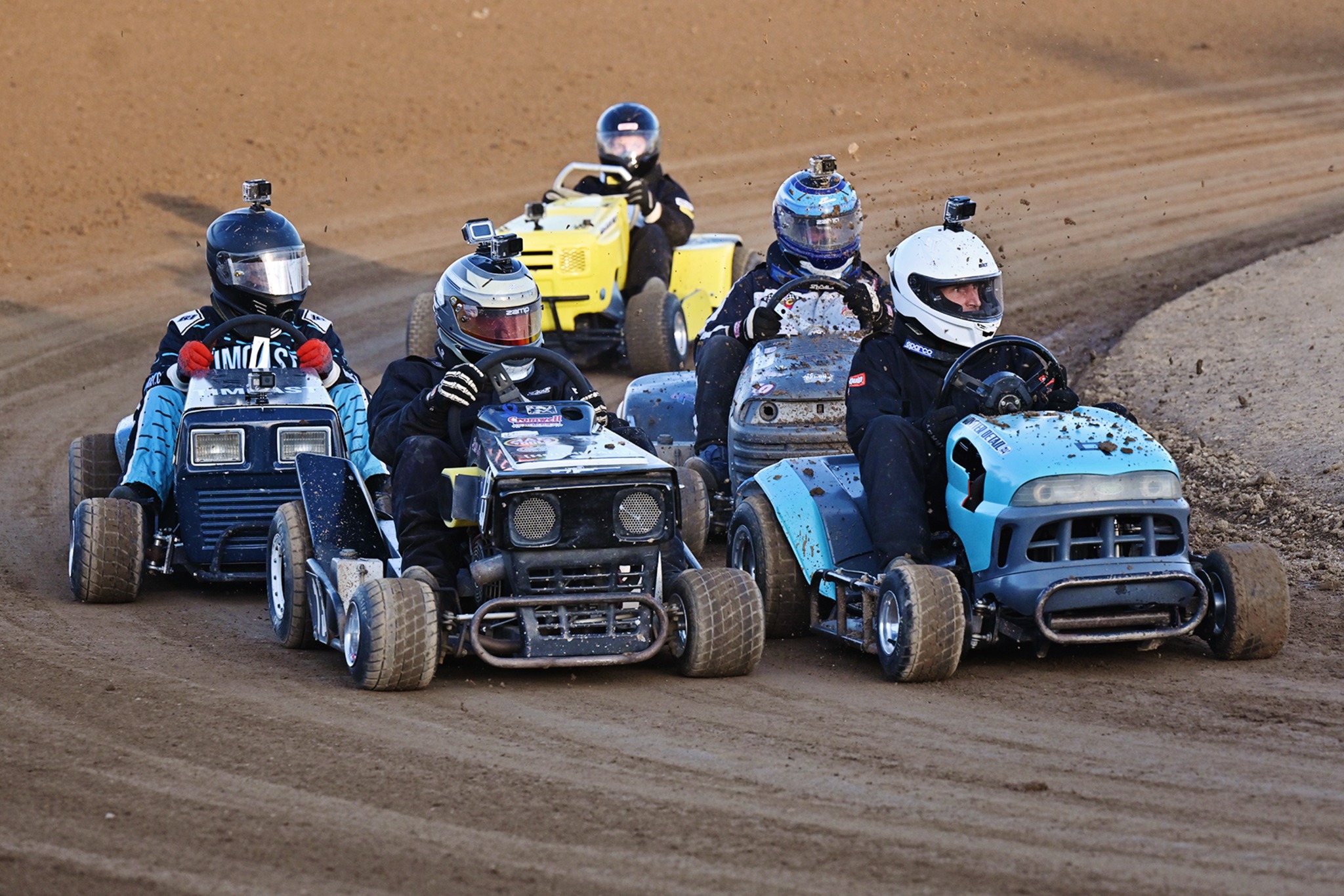 A pack of lawnmower racers racing wheel to wheel on a dirt track